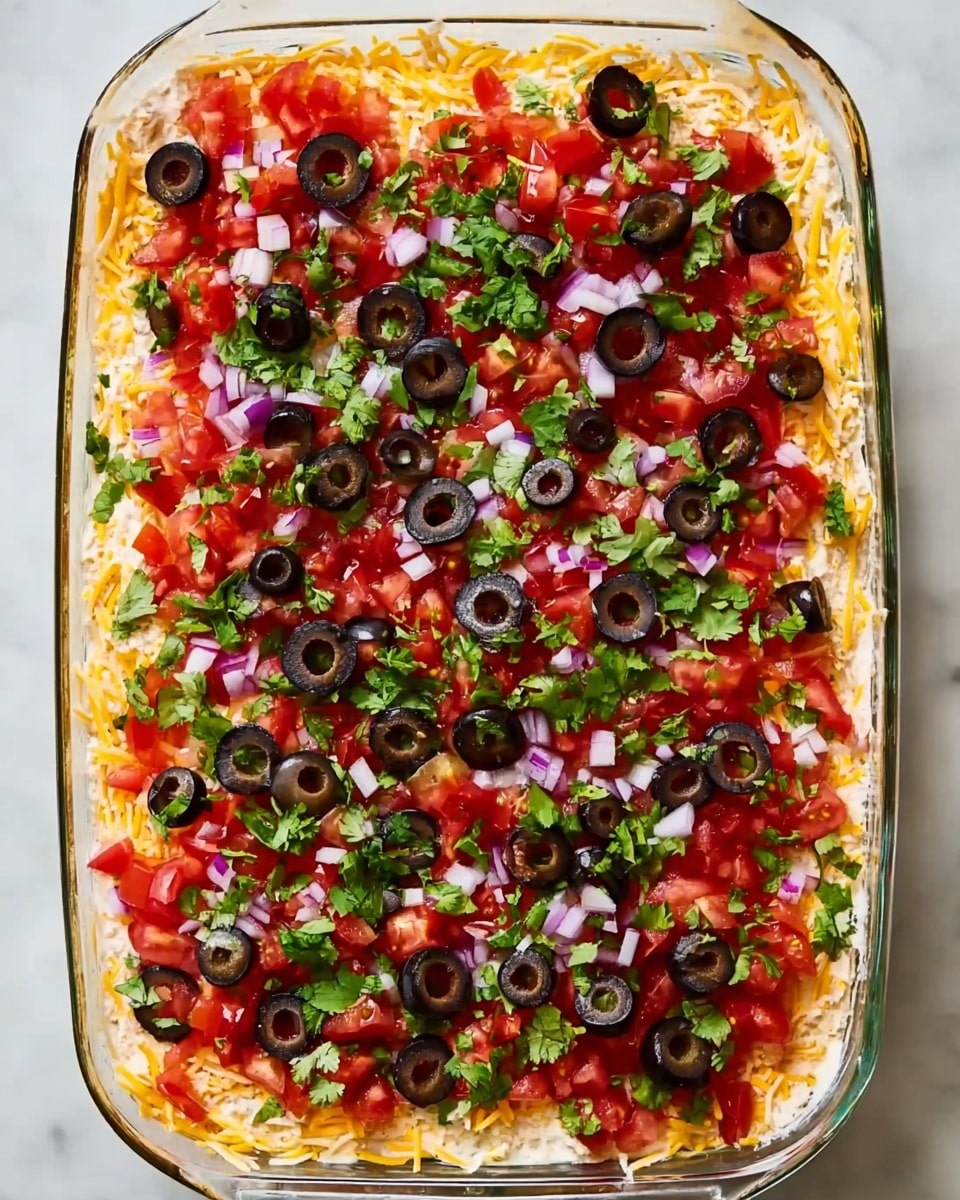 A white rectangular glass dish filled with a layered dip starting with a base of shredded yellow and white cheese spread evenly at the bottom. On top of the cheese, there is a thick layer of chopped fresh red tomatoes mixed with small bits of purple onion and bright green cilantro leaves. The top is covered with sliced black olives scattered across the surface, adding a dark contrast to the colorful vegetables. The dish sits on a white marbled surface. photo taken with an iphone --ar 4:5 --v 7