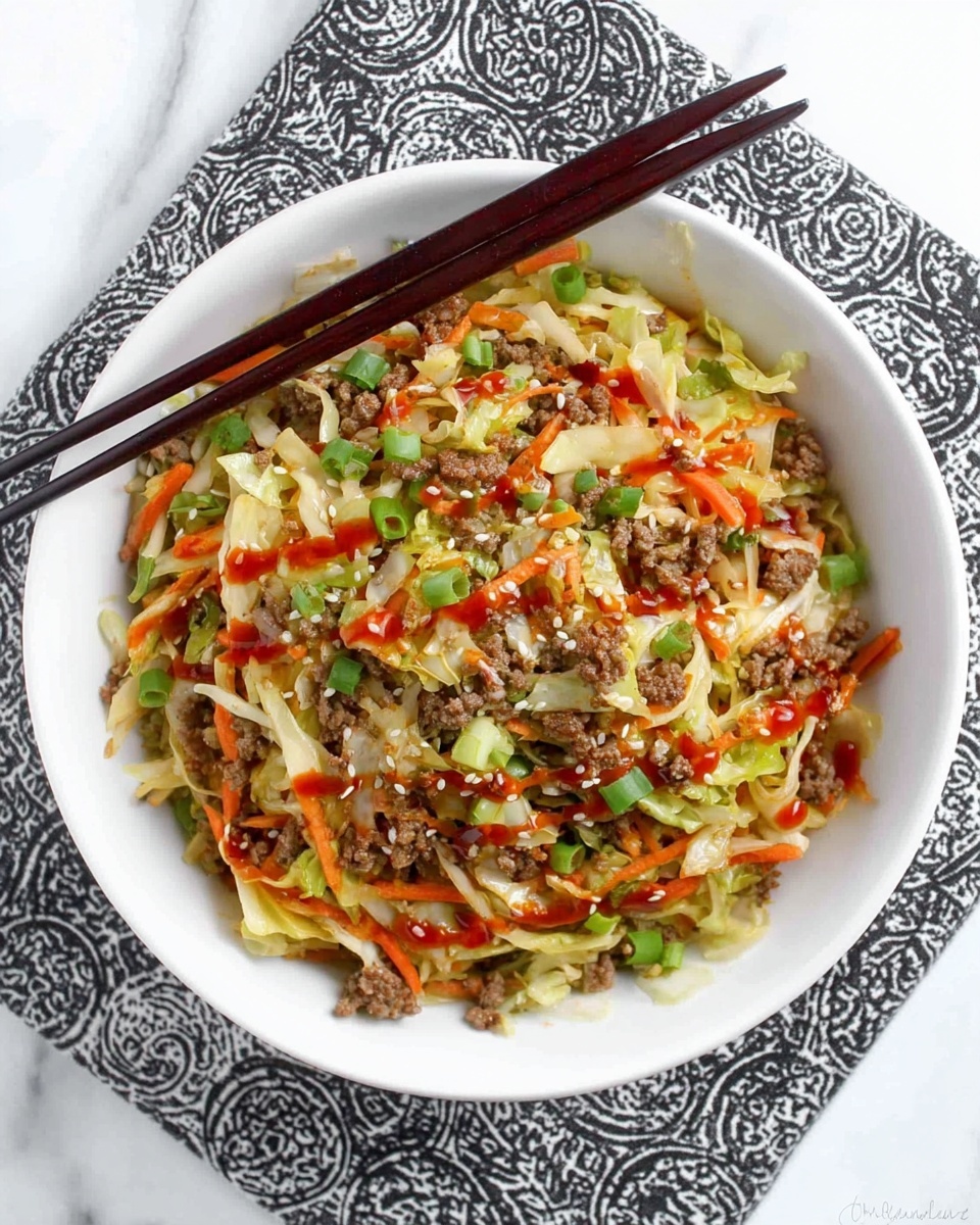 A white bowl filled with a colorful mix of shredded green cabbage, thin carrot strips, and brown cooked ground meat layered evenly throughout. Bright green sliced scallions are sprinkled on top along with small white sesame seeds. A drizzle of red sauce adds a glossy texture and some color contrast over the ingredients. Two dark wooden chopsticks rest on the left edge of the bowl sitting on a patterned black and white cloth, all placed on a white marbled surface. Photo taken with an iphone --ar 4:5 --v 7
