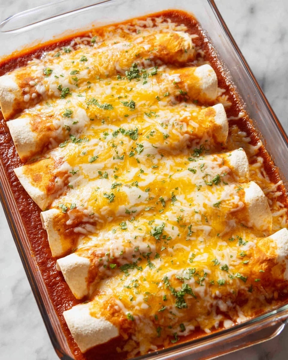A clear glass baking dish holds six rolled tortillas filled with a red tomato sauce layer at the bottom and topped with a melted yellow and white mixed cheese layer. The tortillas are light cream colored with the edges slightly visible under the cheese. Fresh chopped green herbs are sprinkled evenly over the top, adding small, bright green spots on the golden cheese. The dish sits on a white marbled surface, and the photo is taken with an iphone --ar 4:5 --v 7