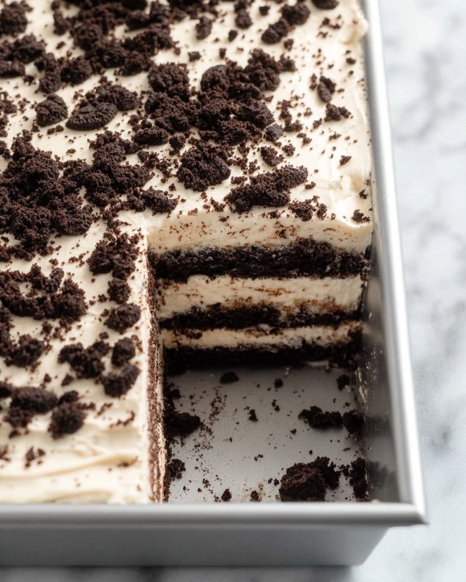 This is a close-up view of a rectangular dessert in a silver baking tray on a white marbled surface. The dessert has multiple visible layers, alternating between creamy white frosting and dark chocolate cookie layers, making about six layers total. The top layer is thick, creamy white frosting sprinkled evenly with crushed dark chocolate cookie pieces. A large square piece has been cut out from the middle right side, showing the clean edges of the layers inside. The whole dessert looks soft and textured with crumbs scattered around the cut edges. photo taken with an iphone --ar 4:5 --v 7