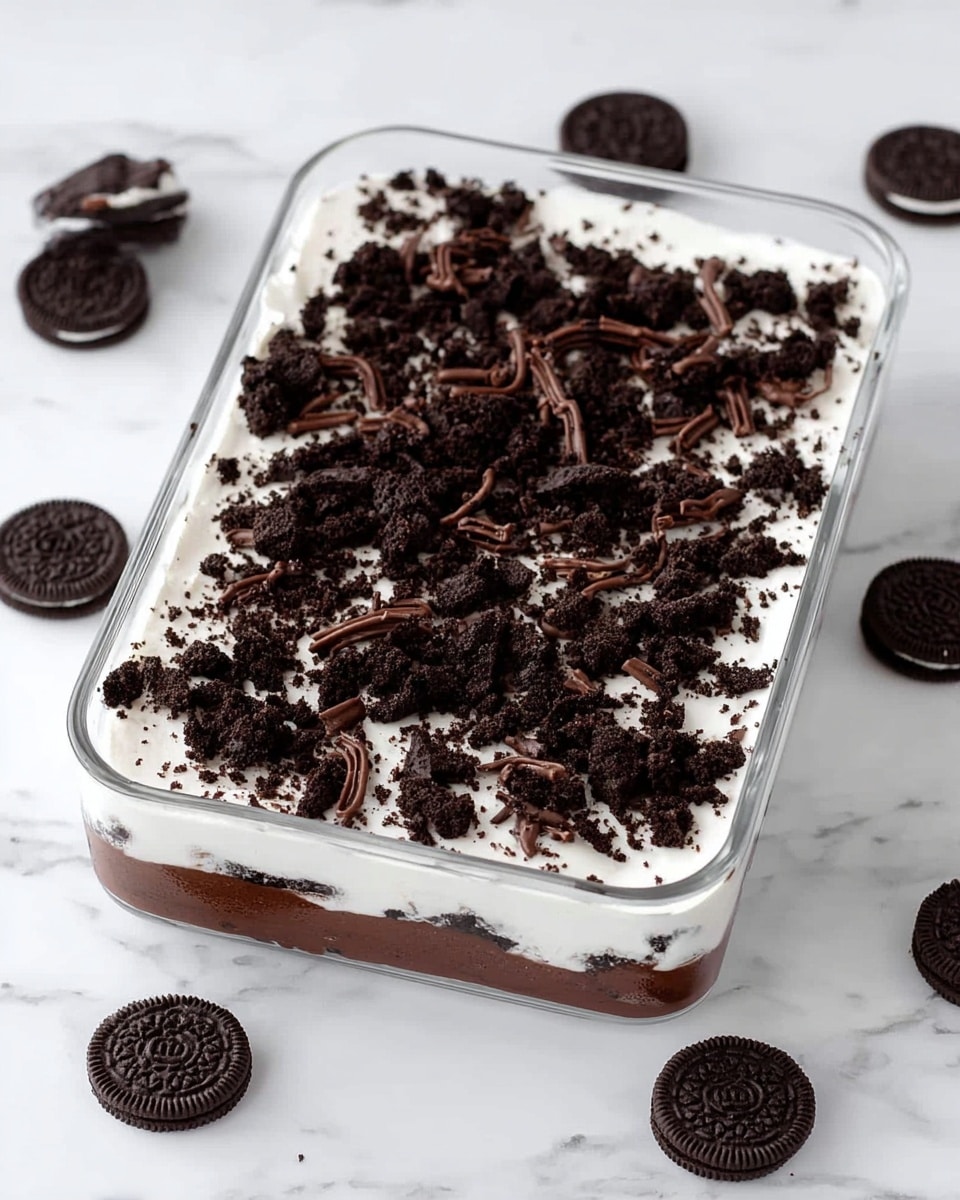 The image shows a rectangular glass dish with a dessert made of three layers: the bottom layer is solid and dark brown, likely crushed chocolate cookies; the middle layer is thick, smooth, and white, probably a cream or pudding; the top layer is made of crumbled dark chocolate cookies mixed with dark chocolate curls scattered evenly across the surface. The dish sits on a white marbled surface with several dark chocolate sandwich cookies placed around it, adding contrast and decoration. photo taken with an iphone --ar 4:5 --v 7