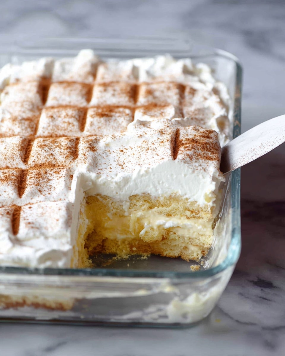 A clear glass dish holds a three-layer dessert on a white marbled surface. The bottom layer is a moist, light yellow cake with a soft texture. Above it is a thick white creamy layer that looks smooth and slightly shiny. The top layer is white whipped cream spread evenly with a light dusting of light brown cinnamon powder on top, creating a grid-like pattern. The dish has a small section missing, revealing the inside layers clearly, and a metal spatula with a white handle rests inside the dish. Photo taken with an iphone --ar 4:5 --v 7