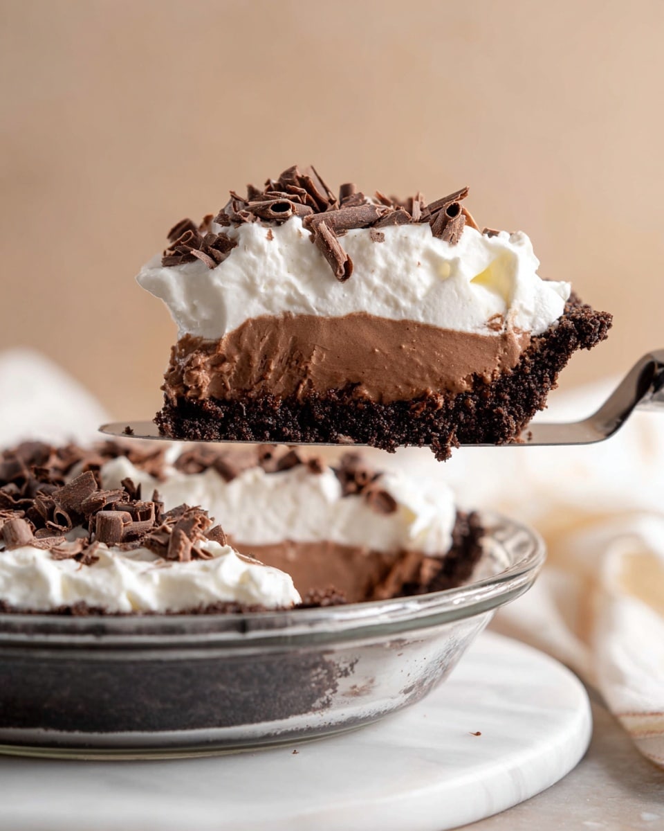 The image shows a slice of chocolate cream pie held by a woman's hand on a pie server above the rest of the pie in a clear glass pie dish. The pie has three visible layers: a thick, dark brown, dense chocolate crust at the bottom, a smooth, lighter brown chocolate cream filling in the middle, and a fluffy white whipped cream topping with dark brown chocolate curls scattered on top. The pie dish sits on a white marbled surface, and the background is a soft beige color. Photo taken with an iphone --ar 4:5 --v 7