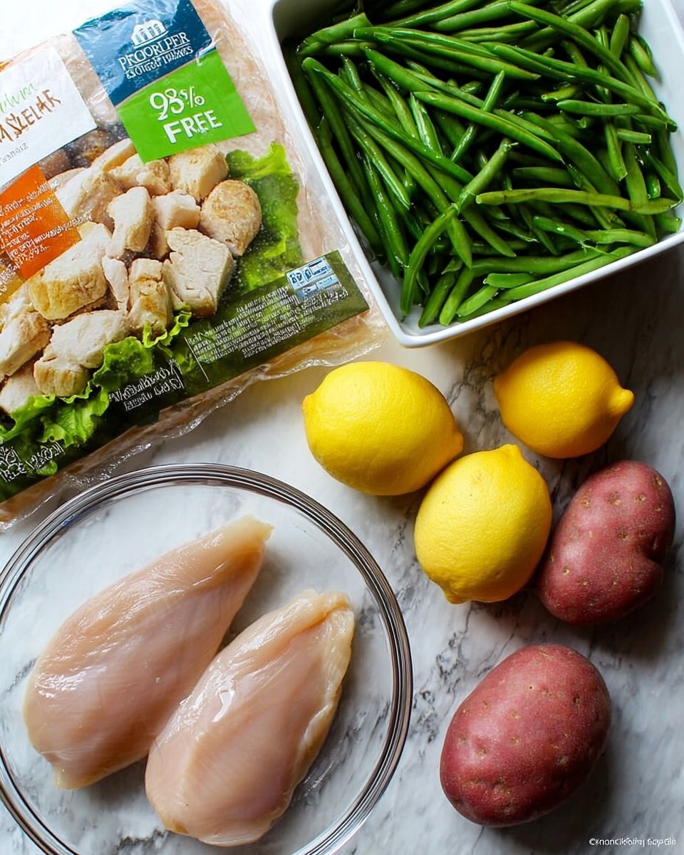 The image shows two raw chicken fillets placed inside a clear glass bowl on the right side of a white marbled surface. Next to it, there is a white container filled with fresh green beans. Above the bowl and container, there are four red potatoes with smooth skin arranged loosely. Two bright yellow lemons sit between the potatoes and the bowl of chicken fillets. On the left side, there is a plastic package with a label showing cooked chicken pieces on a bed of lettuce and a banner that says
