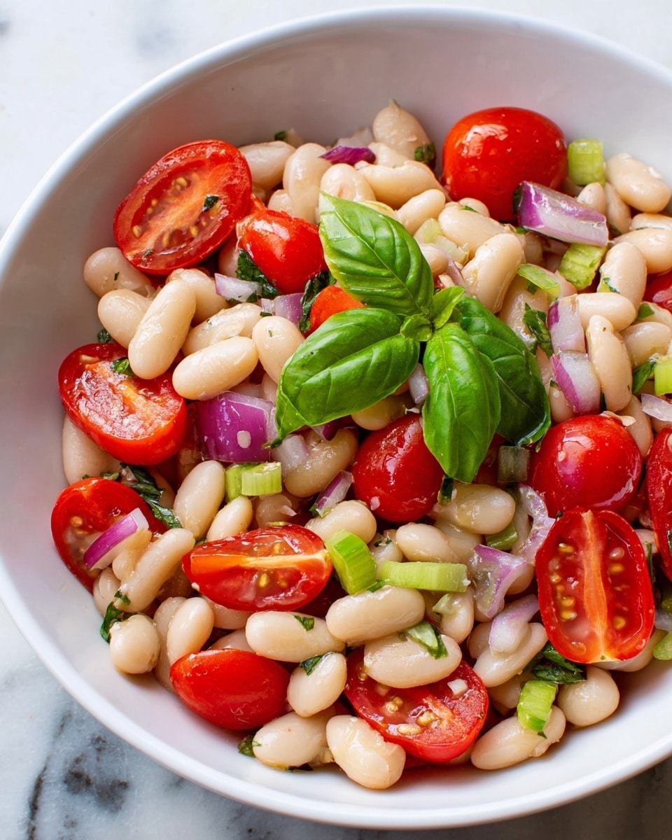A close-up view of a white bowl filled with a fresh salad made of creamy white beans and bright red cherry tomato halves. Small pieces of purple onion and green celery are scattered evenly throughout the salad, adding more color and texture. On top, there is a small bunch of fresh green basil leaves serving as garnish. The bowl is placed on a white marbled surface, with the vibrant colors of the ingredients standing out clearly. photo taken with an iphone --ar 4:5 --v 7