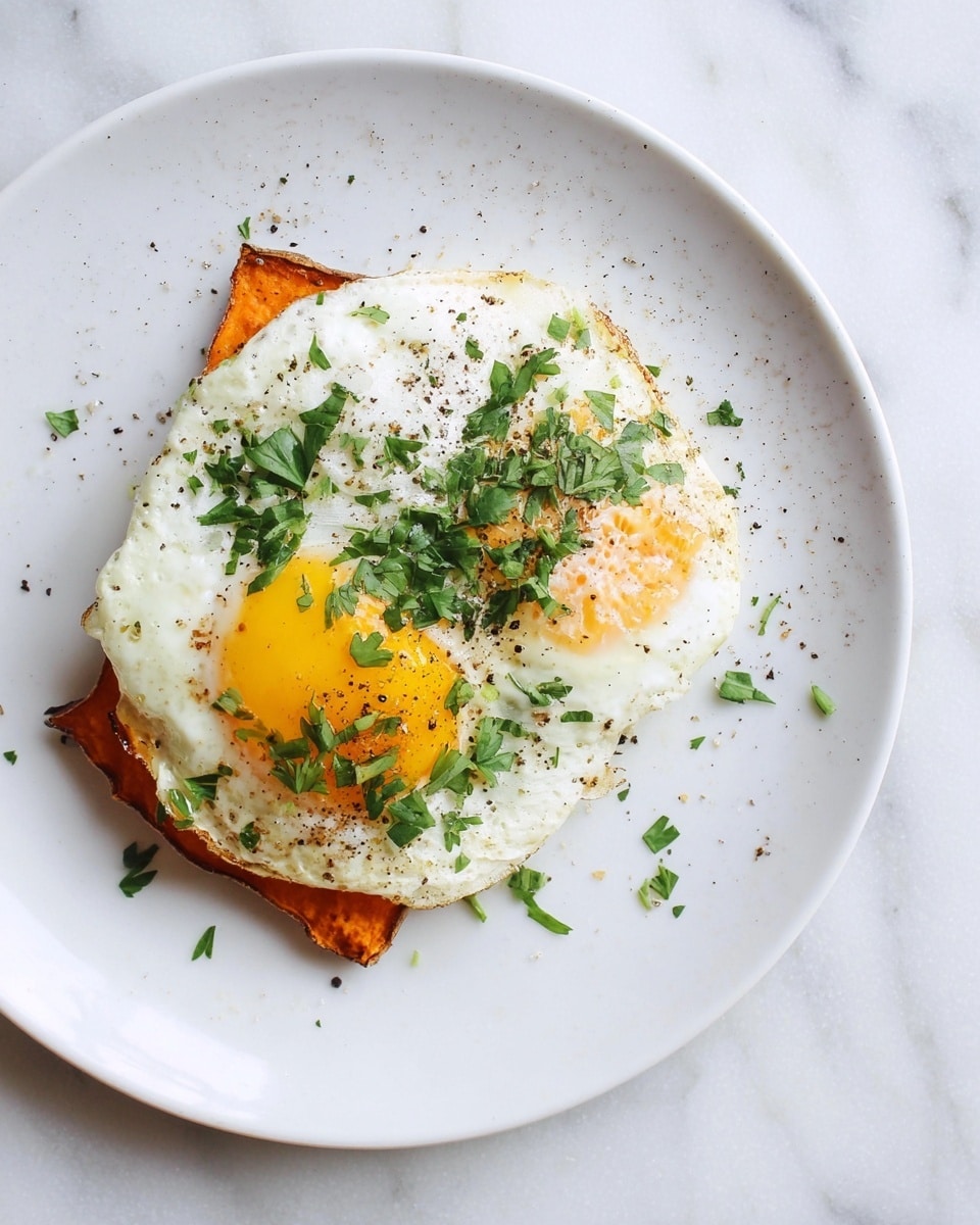 A white plate holds two layers: the bottom layer is a rectangular piece of orange roasted sweet potato with a slightly crispy edge, and the top layer is a sunny-side-up egg with a bright yellow yolk and white edges that softly overlap the sweet potato. The egg is sprinkled with finely chopped fresh green parsley and small black pepper bits. The scene is set on a white marbled surface. photo taken with an iphone --ar 4:5 --v 7