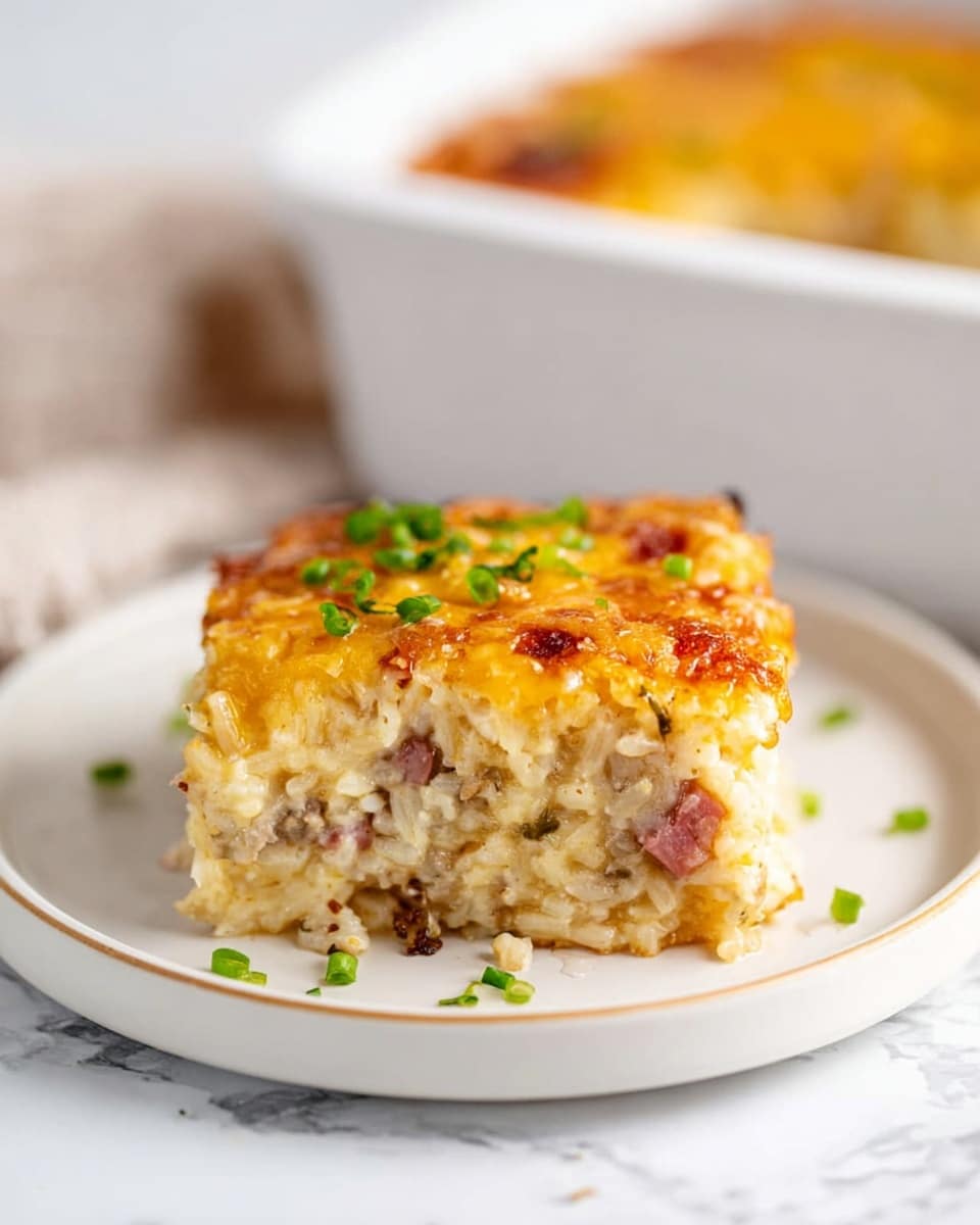 A thick square piece of baked casserole sits on a round white plate on a white marbled surface. The casserole shows three main layers: the bottom and middle layers are creamy and textured, filled with rice and small chunks of pinkish meat mixed throughout. The top layer is golden brown melted cheese with some green chopped scallions scattered over it. The casserole looks soft inside with a slightly crispy top and a moist, rich filling. In the background, the white baking dish holding the casserole is partly visible. photo taken with an iphone --ar 4:5 --v 7