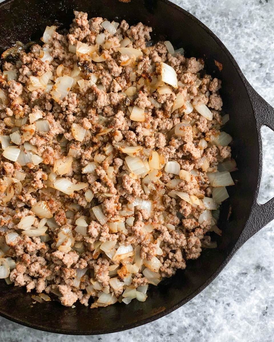 A close-up top view of a black cast iron pan filled with cooked ground meat mixed with small white and translucent chopped onions, showing a mix of light brown and beige colors, with the pan resting on a white marbled texture surface photo taken with an iphone --ar 4:5 --v 7