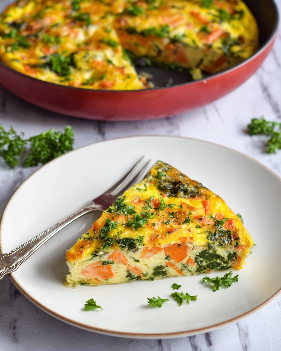 A slice of frittata sits on a white plate with a vintage silver fork beside it, showing three layers: a light yellow egg base with orange carrot pieces, green spinach leaves, and scattered small green parsley leaves on top. In the background, the rest of the frittata is visible in a round red pan, showing a thick, golden-yellow top with the same vegetables and herbs spread throughout. The whole scene rests on a white marbled texture surface. Photo taken with an iphone --ar 4:5 --v 7