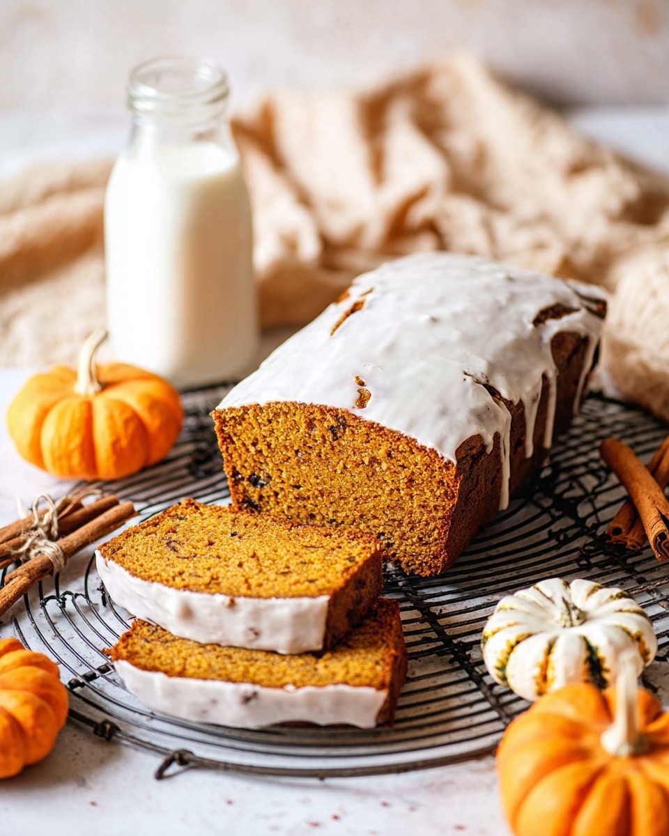 The image shows a loaf of pumpkin bread with white icing on top, placed on a round black cooling rack over a white marbled surface. The loaf is thick and golden brown with a moist texture. Two slices of pumpkin bread are cut and placed in front of the loaf, showing the same golden brown inside and white icing on the lower side of one slice. Surrounding the bread are small orange and white pumpkins, cinnamon sticks, and a clear glass bottle filled with milk. A beige cloth is softly spread in the background, adding a cozy touch. Photo taken with an iphone --ar 4:5 --v 7