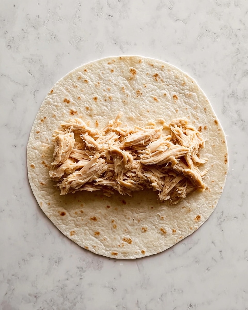 A round soft tortilla is placed flat on a white marbled surface. On top of the tortilla, there is a layer of green, fresh, and crisp shredded lettuce spread mostly in the center. Above the lettuce, there is a generous amount of shredded seasoned chicken piled in the middle, with thin slices of light purple onion scattered over the chicken. Bright red halved cherry tomatoes are placed on top and around the chicken and lettuce, adding vibrant color to the wrap photo taken with an iphone --ar 4:5 --v 7