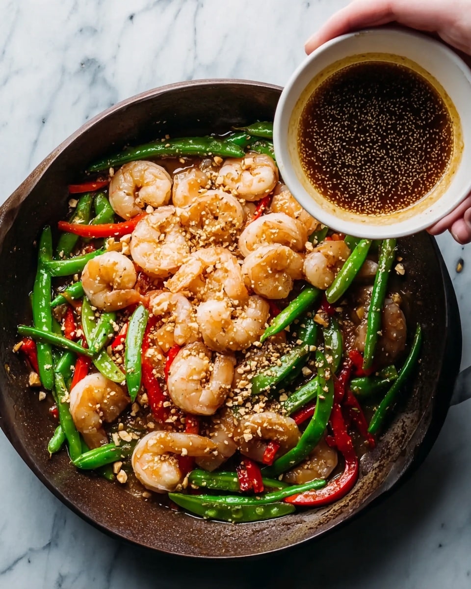The image shows a dark pan filled with cooked shrimp, bright green snap peas, and red pepper strips mixed together. The shrimp are pale pink and curled, sitting at the bottom and middle of the pan. The snap peas and red pepper pieces add pops of green and red on top and around the shrimp. There are small bits of crushed nuts sprinkled across the dish, adding a light crunchy texture. A woman’s hand holds a white bowl above the pan, pouring a dark brown sauce with sesame seeds over the shrimp and vegetables. The surface under the pan is a white marbled texture. photo taken with an iphone --ar 4:5 --v 7