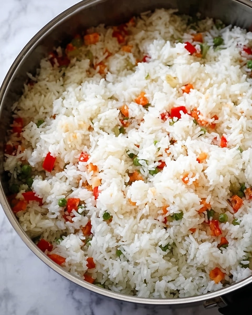 A close-up image shows a metal pan filled with cooked white rice mixed with small pieces of red bell pepper, green peas, and bits of onion. The rice layer looks fluffy and soft, covering the colorful vegetables underneath. The pan sits on a white marbled surface, and the overall look is fresh and simple. photo taken with an iphone --ar 4:5 --v 7