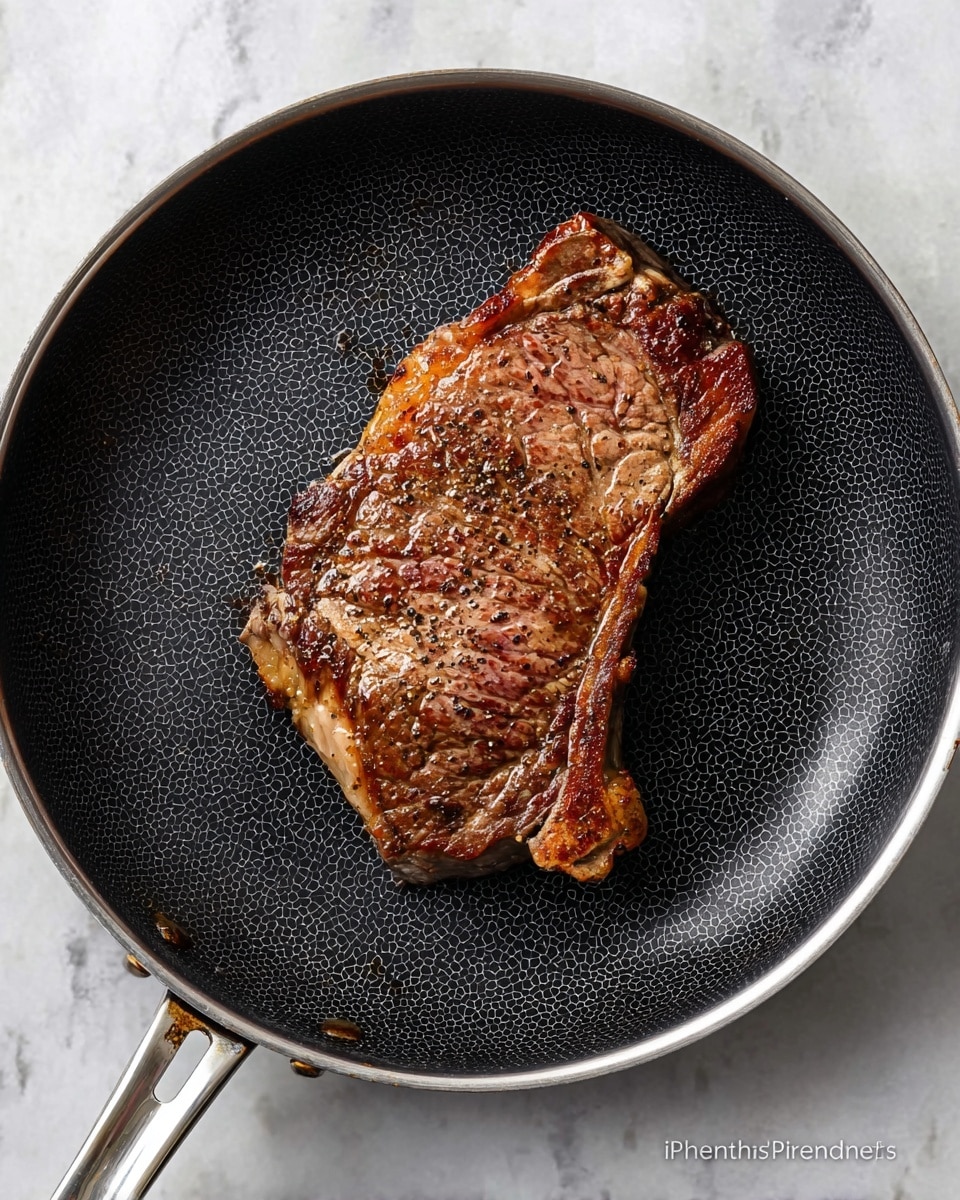 A single large piece of cooked steak with a browned and slightly crispy surface lies flat in the middle of a black frying pan with a honeycomb pattern. The steak shows a mix of dark brown seared areas and lighter spots, with visible seasoning of black pepper. The pan has a shiny silver handle extending from the left. The background is a white marbled texture. photo taken with an iphone --ar 4:5 --v 7