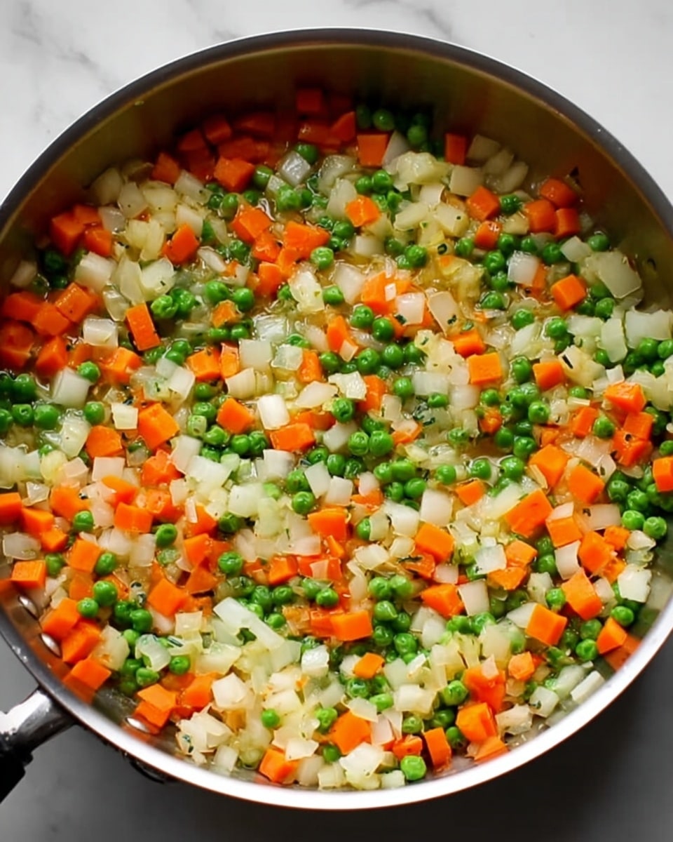 A close-up of a cooking pan filled with small diced white onions, bright orange carrots, and fresh green peas evenly spread across the pan's surface. The onions are chopped into medium-sized pieces, the carrots are in small cubes, and the peas are whole and round, creating a colorful and vibrant mix. The pan has a shiny silver surface with a black handle, sitting on a clean white marbled background. photo taken with an iphone --ar 4:5 --v 7