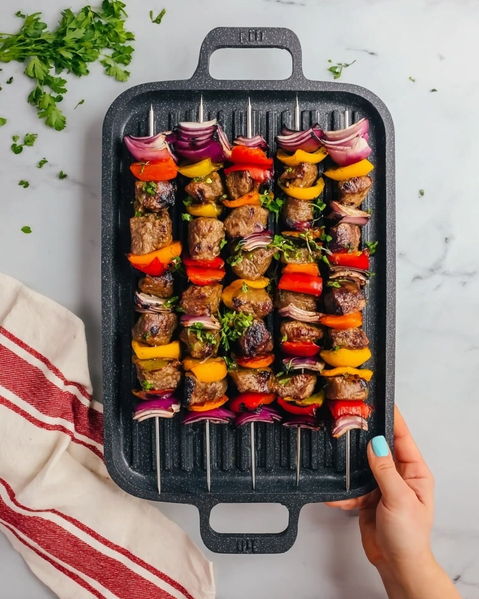 The image shows a black grill pan held by a woman's hands with light blue nail polish, against a white marbled surface with a red-striped white cloth and some green herbs scattered nearby. On the pan, there are five skewers lined up horizontally, each loaded with several chunks of grilled brown meat, alternating with red, yellow, and orange bell pepper pieces and some slightly charred red onion slices. Small green herb leaves are sprinkled on the skewers and pan. The grill pan has a rough texture and two handles, one on each side. photo taken with an iphone --ar 4:5 --v 7