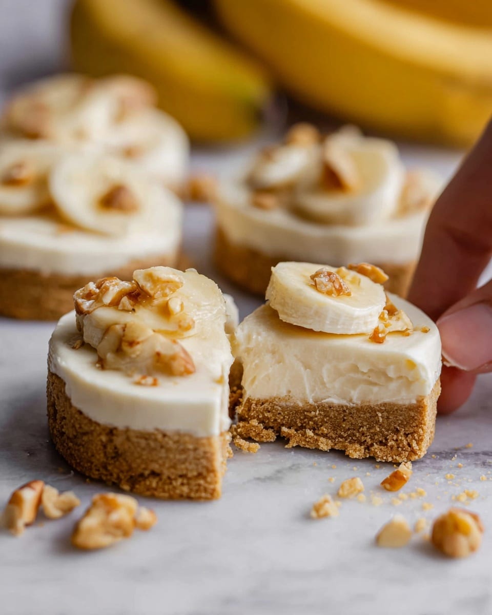 The image shows a close-up of round cookies with two layers: a thick, crumbly light brown base and a smooth, creamy off-white top layer. Each cookie is decorated with small banana slices and broken golden brown nut pieces placed on top. One cookie is cut in half, with the woman’s hand holding one part, revealing the thickness and texture of both layers. The cookies are placed on a white marbled surface, with a bunch of bananas blurred in the background. Crumbs and bits are scattered around the cookies, giving a fresh and homemade feel. photo taken with an iphone --ar 4:5 --v 7