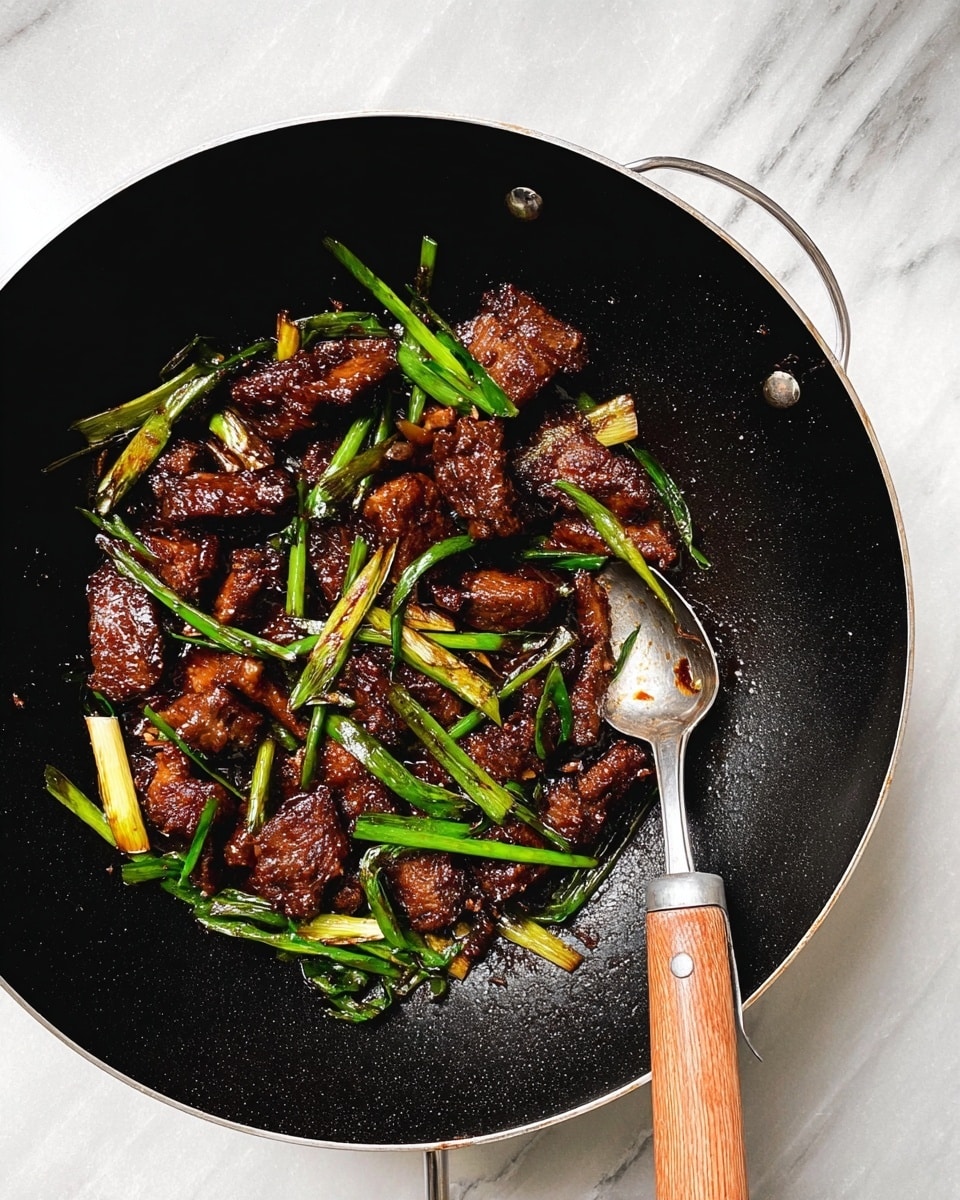 The image shows a black wok with a wooden handle filled with dark brown cooked meat pieces mixed with bright green sliced scallions. The meat looks crispy and has a shiny texture from a thick sauce. A silver spoon is placed inside the wok, resting on the cooked food. The wok is placed on a white marbled surface. photo taken with an iphone --ar 4:5 --v 7