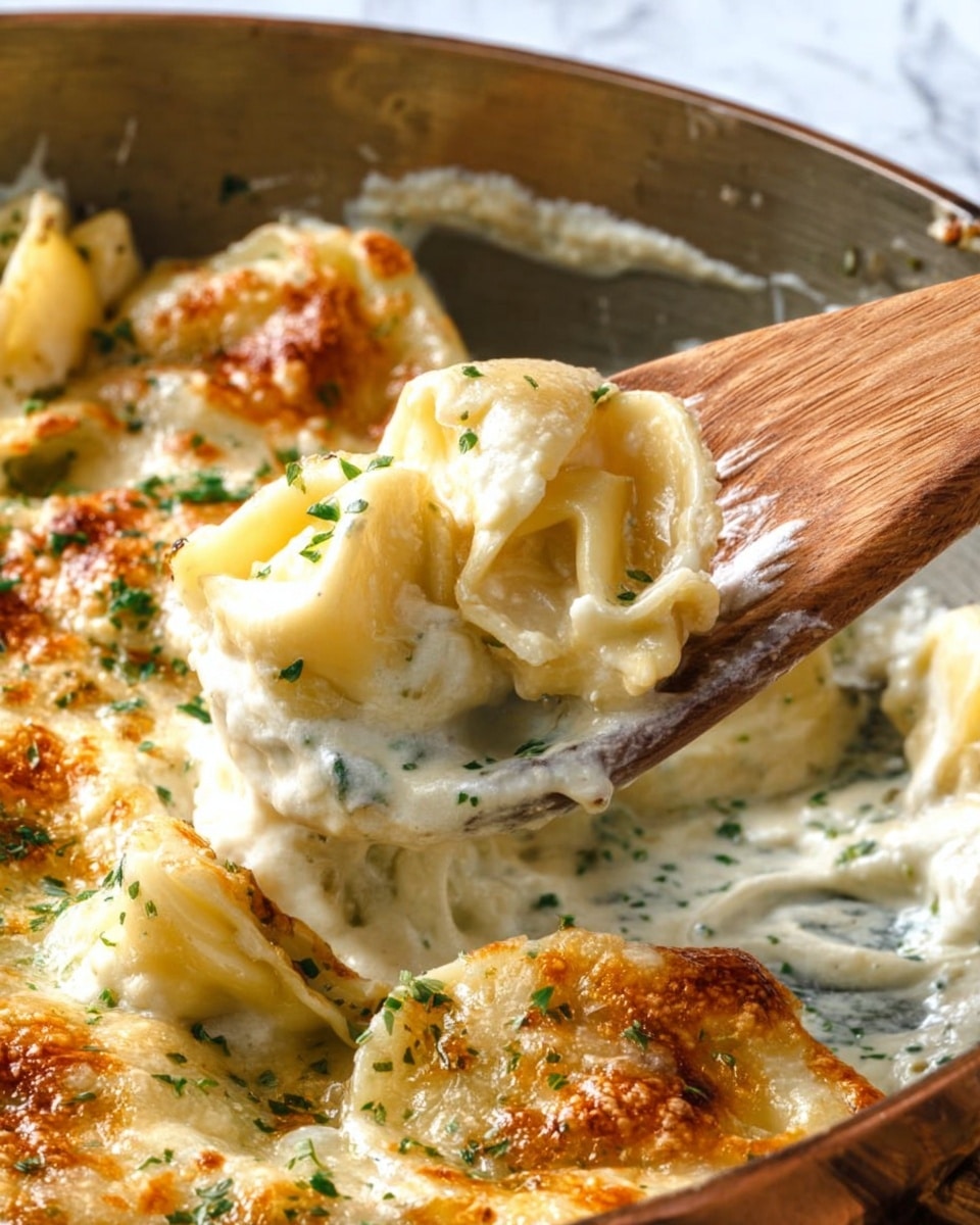 The image shows a close-up of creamy tortellini in a metal baking dish with a golden brown cheese crust on top. The tortellini are pale yellow and covered in a smooth white sauce with some green herb bits sprinkled over it. A wooden spoon lifts one piece of tortellini from the dish, showing the creamy filling inside. The edges have a slightly crispy texture with browned spots, and the white sauce looks thick and rich around the pasta. The background is changed to a white marbled texture. photo taken with an iphone --ar 4:5 --v 7
