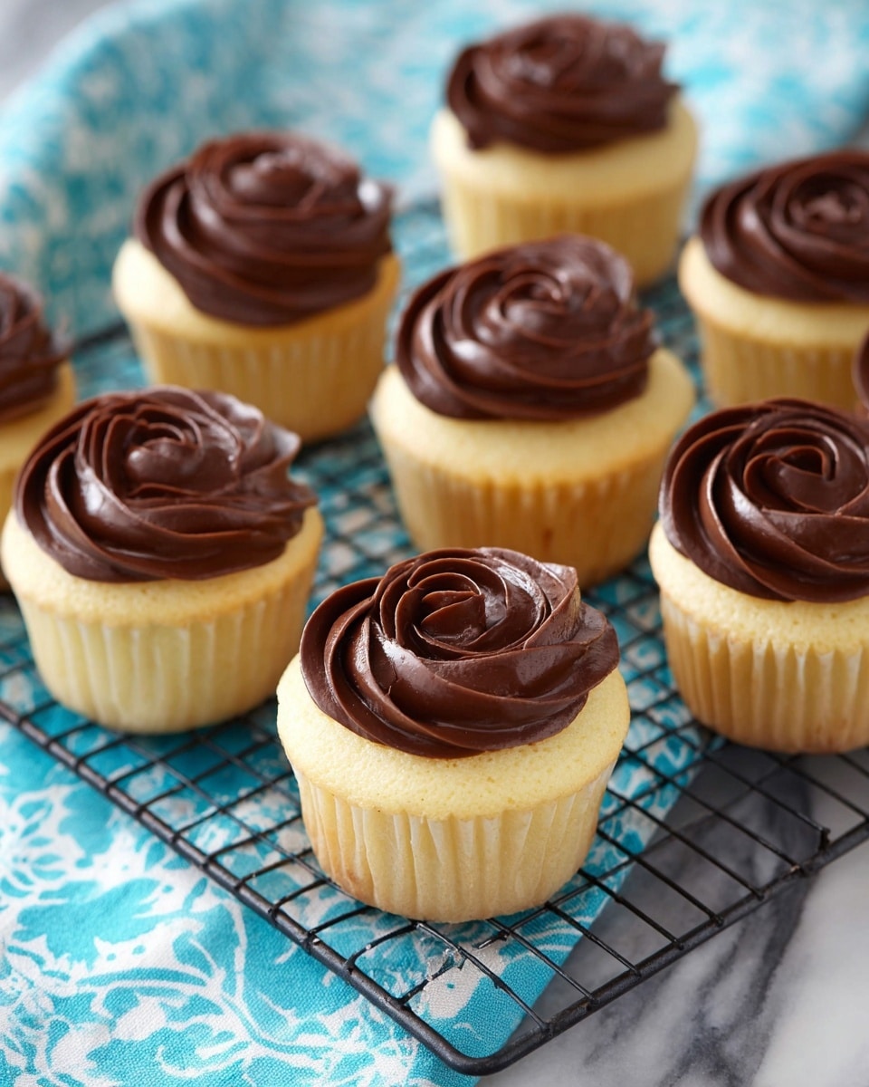 There are seven cupcakes arranged on a black cooling rack over a white marbled surface with a blue and white cloth underneath. Each cupcake has two layers: a light yellow cake base wrapped with a white paper liner, topped with a swirl of smooth dark chocolate frosting that has a shiny, rich texture, designed to look like a rose on top. The cupcakes are evenly spaced, showing the soft texture of the cake beneath the thick, glossy chocolate frosting. photo taken with an iphone --ar 4:5 --v 7