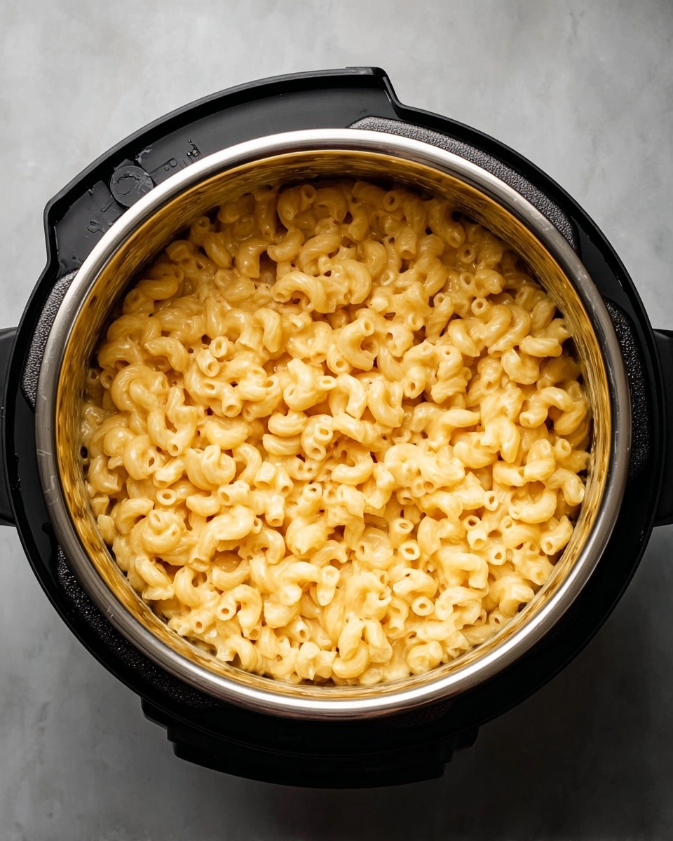 A metal pot filled with one layer of creamy, light yellow macaroni and cheese pasta. The macaroni shapes are small and curved, coated evenly with a smooth cheese sauce. The pot sits on a white marbled surface, and the photo is taken from above showing the whole pot and its black handles. The lighting highlights the glossy texture of the sauce and the soft shapes of the pasta photo taken with an iphone --ar 4:5 --v 7