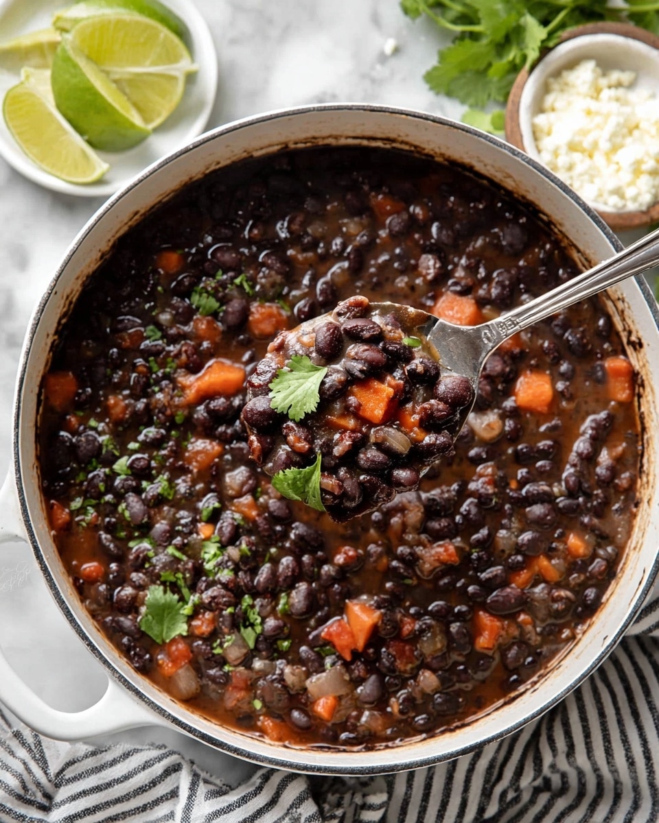 A white pot filled with dark black beans cooked with chunks of soft orange carrots and small bits of onion visible. The surface is thick and slightly shiny with a few sprigs of fresh green cilantro placed on top for garnish. A silver spoon lifts a scoop of beans, showing the hearty texture and mix of colors. Around the pot, there are lime wedges on a white plate and a small white bowl of crumbly white cheese placed on a white marbled surface. A striped cloth is partially visible next to the pot. Photo taken with an iphone --ar 4:5 --v 7