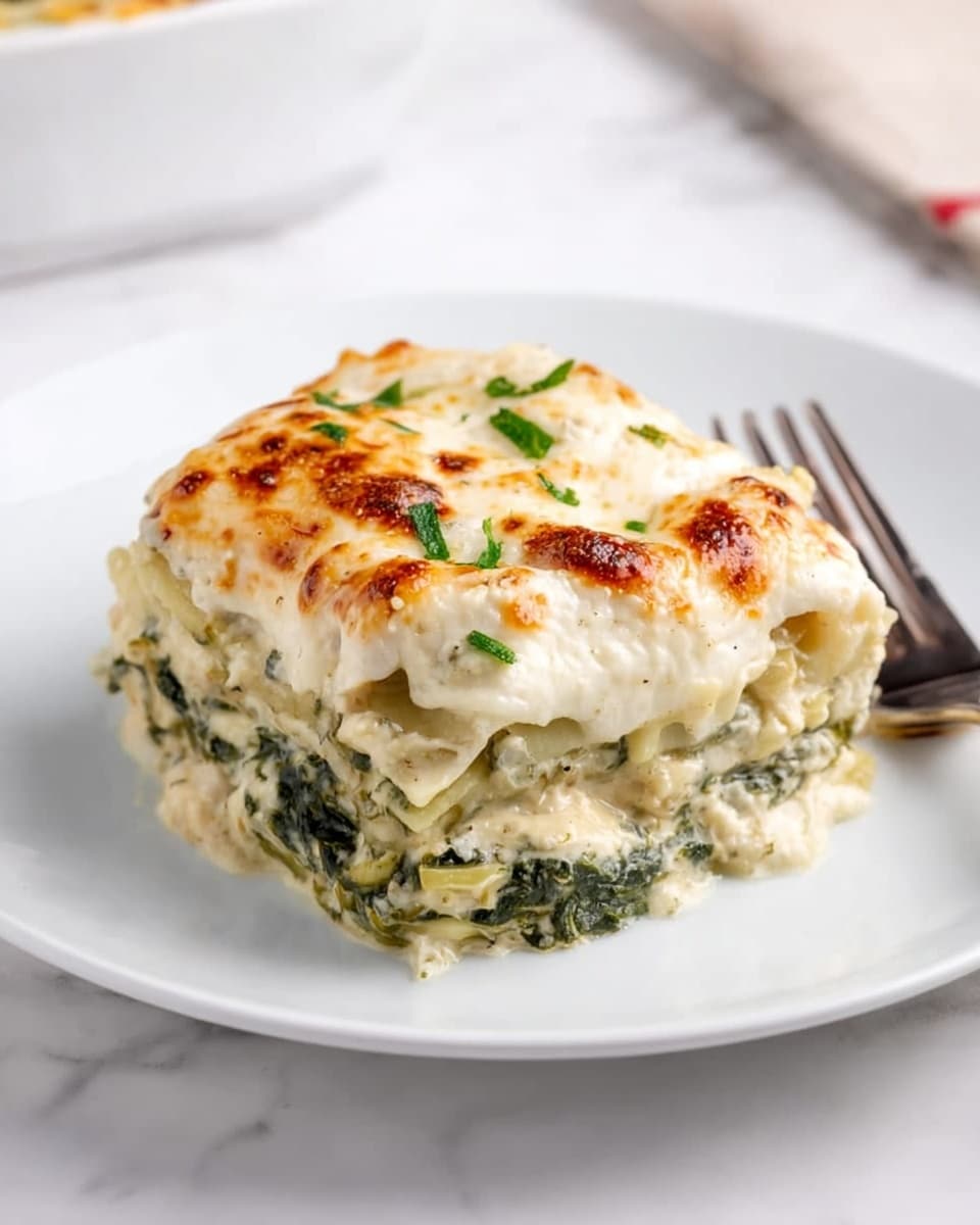 A thick slice of creamy lasagna is placed in the center of a white plate, showing about four visible layers. The bottom layer is pale yellow pasta followed by a thick layer of cooked green spinach mixed with white sauce. Above this is another pasta layer topped with a rich, bubbly white cheese sauce that has some lightly browned spots and is sprinkled with small green herbs. The edges of the lasagna look soft and slightly melted, with the whole dish having a smooth, rich texture. The plate sits on a white marbled surface, next to a silver fork on the right side. Photo taken with an iphone --ar 4:5 --v 7