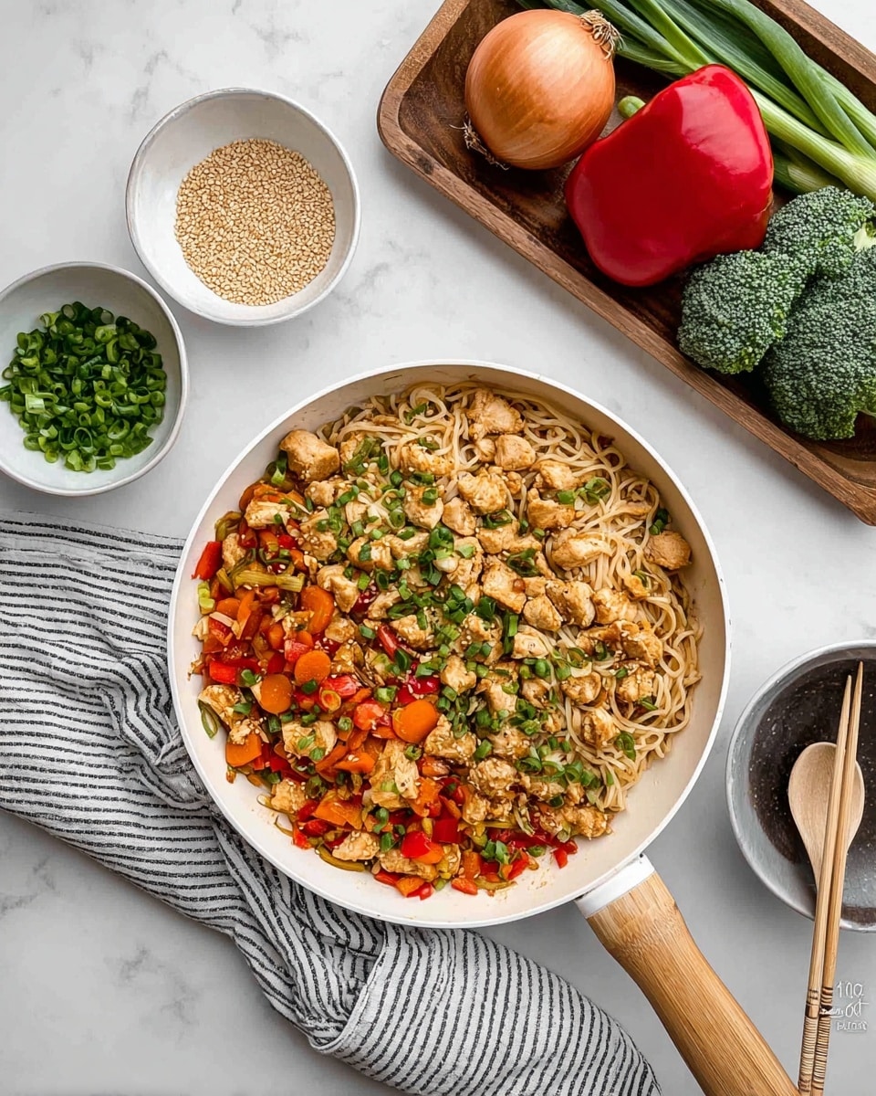 A white pan filled with three layers of food: the bottom layer is light brown cooked noodles, the middle layer has mixed vegetables including orange carrot strips, and red bell pepper pieces, and the top layer has chopped light brown cooked chicken pieces with small green onion slices sprinkled all over. Next to the pan are two small bowls, one with sesame seeds and the other with chopped green onions. To the top right, a wooden tray holds a whole round onion, red bell pepper, broccoli, and several green onions. At the bottom right corner, a white bowl with a dark rim holds two wooden chopsticks. Everything is placed on a white marbled surface with a striped cloth under the pan’s wooden handle. Photo taken with an iphone --ar 4:5 --v 7