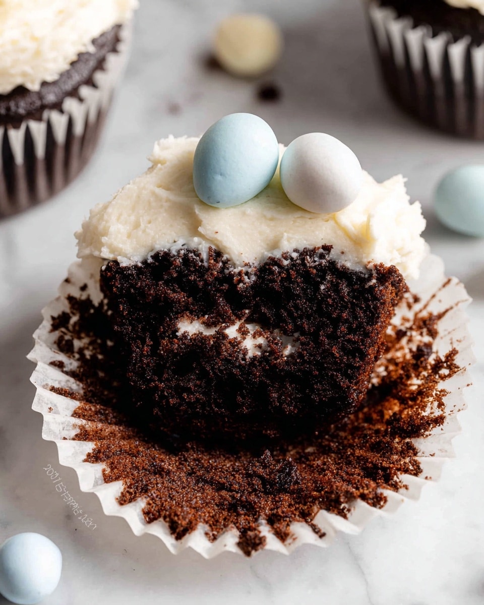 A close-up of a chocolate cupcake with three visible layers: the bottom layer is a dark, moist chocolate cake with rich texture; the middle layer is a thick, creamy white frosting spread unevenly over the cake; the top layer has two small, smooth candy eggs colored light blue and white resting on the frosting. The cupcake is in a white paper liner with chocolate crumbs stuck to the sides. The cupcake sits on a white marbled surface with some pastel-colored candy eggs scattered nearby. Photo taken with an iphone --ar 4:5 --v 7