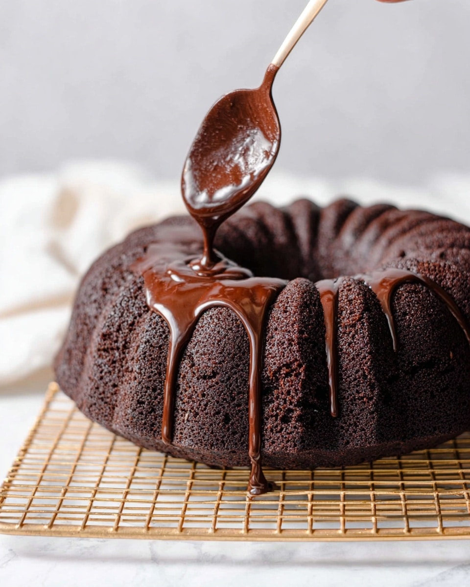 A dark brown chocolate bundt cake is placed on a gold cooling rack above a white marbled surface. The cake's outer layer looks slightly rough and dense with deep ridges around its ring shape. A spoon held by a woman's hand is pouring shiny, smooth, thick chocolate glaze over the top, dripping down the ridges in thick ribbons. The background is soft and white, making the rich colors of the cake and glaze stand out clearly. photo taken with an iphone --ar 4:5 --v 7